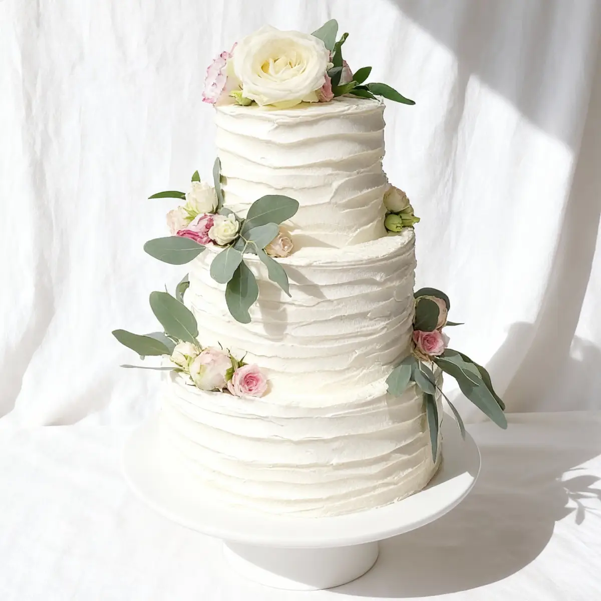 Tort weselny w kolorze białym, ozdobiony różami, zielonymi liściami, wykonany w Pracowni Torty Złote – Iwona Pasternak-Karaś (Gryfice)